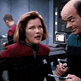a bald man is talking to a woman in a red jacket