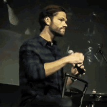 a man in a plaid shirt holds a microphone in his right hand