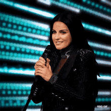 a woman in a black jacket is holding a microphone in front of a blue background