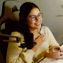 a woman wearing glasses is smiling in front of a microphone while holding a cup of coffee