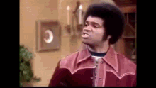a man with an afro is wearing a red leather jacket and making a funny face .