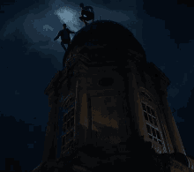 two men are standing on top of a very tall building at night