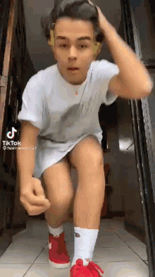 a young man in a white shirt and red shoes is kneeling down on the floor .