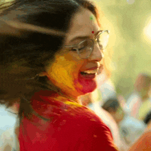 a woman wearing glasses and a red shirt is covered in red and yellow powder