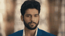 a man with a beard and a blue suit looks at the camera