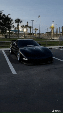 a black sports car is parked in a parking lot in front of a park