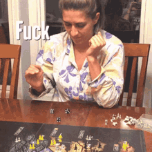 a woman sits at a table playing a board game with the word fuck above her head