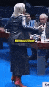 a woman in a black leather jacket and red boots stands in front of a table with a sign that says se on it