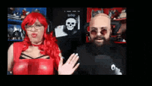 a man with a beard and a woman with red hair are standing next to each other and waving .