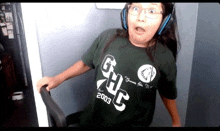 a girl wearing headphones and a green t-shirt with the year 2003 on it is sitting in a chair .