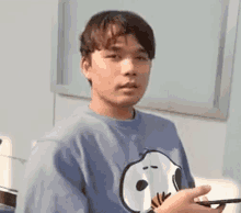 a man wearing a blue snoopy t-shirt is holding a cell phone in his hand .