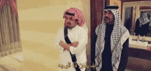 two men are standing next to each other in a room with arabic writing on the wall .