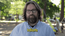 a man with glasses and a beard says idiots in yellow letters