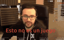 a man with glasses and headphones is sitting in front of a screen that says " esto no es un juego "