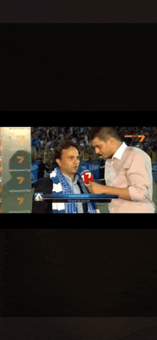 a man with a scarf around his neck is being interviewed by a man with a microphone