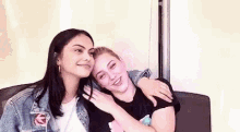 two young women are sitting next to each other on a couch and hugging each other .