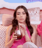 a woman in a pink dress is sitting on a couch drinking from a glass with a straw .