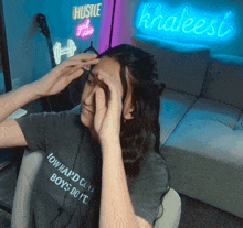 a woman adjusts her hair in front of a neon sign that reads hustle