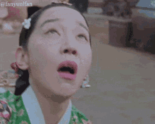 a close up of a woman 's face with her mouth open and a flower in her hair .