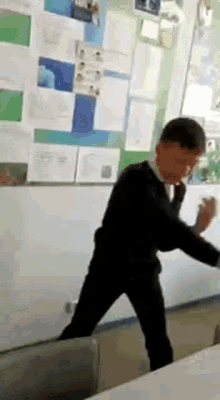 a boy in a suit and tie is standing in a classroom in front of a wall .