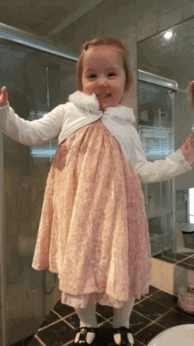a little girl wearing a pink dress and a white jacket smiles for the camera