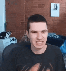 a man in a black shirt is making a funny face in a room with a cat .