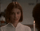 a woman in a white shirt looks at a man with a candle in the background