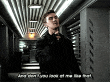 a man in a black jacket is standing in a hallway and says " and don 't you look at me like that "