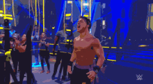 a shirtless wrestler stands in front of a crowd with a w logo in the background