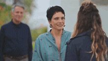 a woman in a blue shirt is talking to another woman while a man stands in the background .