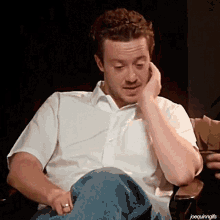 a man in a white shirt sits in a chair with his hand on his face