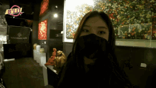 a woman wearing a black mask stands in front of a sign that says a.c.c. design house