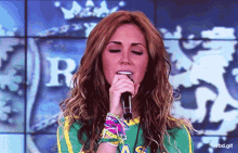a woman singing into a microphone in front of a shield with the letter r on it