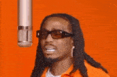 a man with dreadlocks is singing into a microphone while wearing sunglasses .