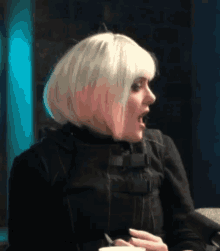 a woman with blonde hair and a black jacket is holding a cup of coffee