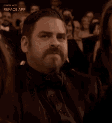 a man with a beard and bow tie is sitting in a crowd of people clapping .
