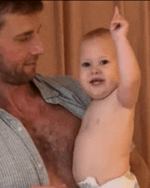 a man is holding a baby in his arms and the baby is making a funny face .