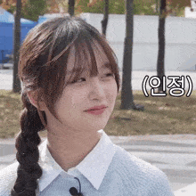 a girl with a braided ponytail looks at the camera in front of a foreign language sign