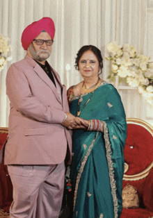 a man in a pink suit and turban holds hands with a woman in a green dress