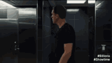 a man in a black shirt is standing in a bathroom looking at himself in a mirror .