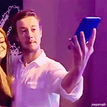 a man in a white shirt is taking a selfie with a blue cell phone with joequinngifs written below him