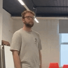 a man wearing glasses and a gray shirt is standing in a room .
