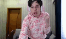 a young man wearing headphones and a pink sweater is standing in a room .