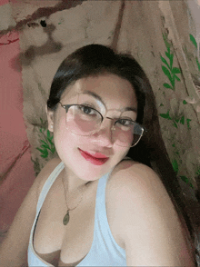 a woman wearing glasses and a white tank top is smiling for the camera