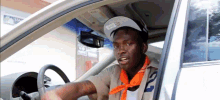 a man wearing a hat and an orange bandana is driving a car
