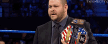 a man in a suit and tie is holding a wrestling championship belt in a ring .