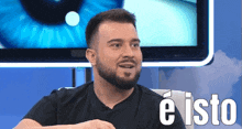 a man with a beard says e isto in front of a tv screen