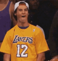 a man wearing a lakers jersey and a hat is sitting in the stands .
