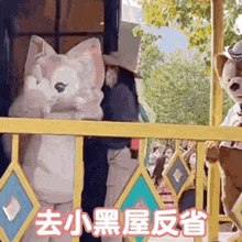 a teddy bear in a costume is standing behind a yellow fence with chinese writing on it .