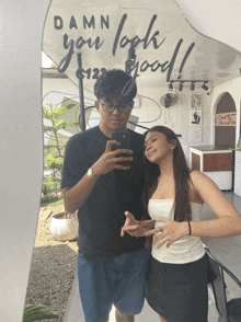 a man and a woman are taking a picture in front of a mirror that says damn you look good
